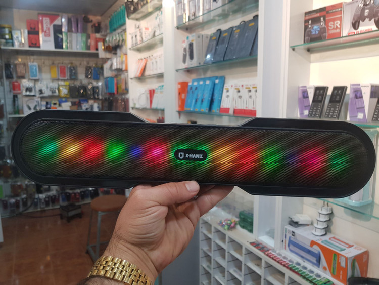 نمای نزدیک از اسپیکر پرتابل X-HANZ C18 با جلوه نور RGB در دست مشتری در فروشگاه مُجیتِل